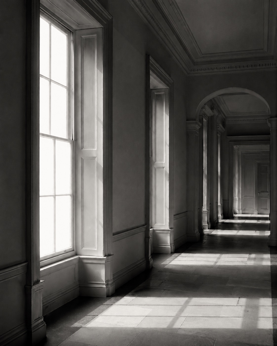 An empty corridor in a historic institutional building, with daylight falling across a stone floor.